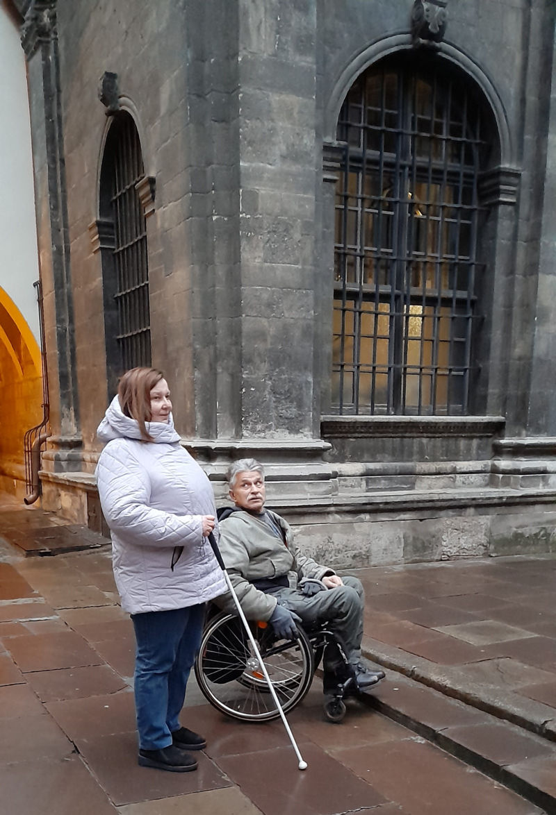 Людина з тростиною та людина в кріслі колісному перед сходинкою на подвірʼї церкви